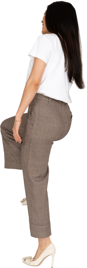 Three-quarter back view of young lady in breeches and t-shirt raising leg