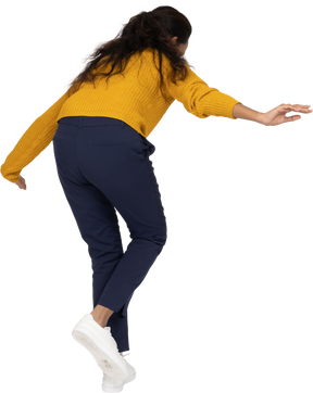 Rear view of a girl in casual clothes posing on one leg with outstretched arms