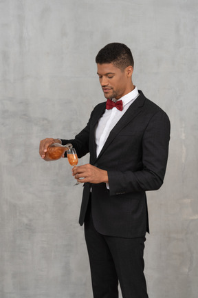 Homem com roupa formal despejando espíritos em um copo de flauta