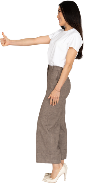 Side view of a smiling young lady in breeches and t-shirt showing thumb up