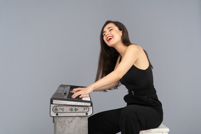 Side view of a smiling sitting young lady in black suit while playing the piano