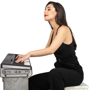 Side view of a smiling young lady in black suit sitting and playing the piano
