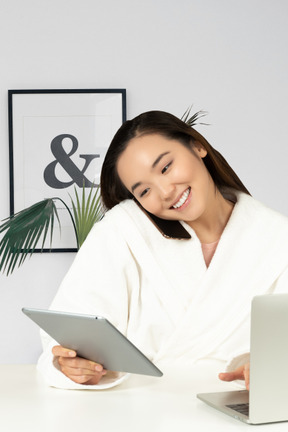 Woman in bathrobe sitting at table with laptop and talking on the phone
