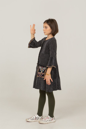 Three-quarter view of a little girl in dress showing ok gesture