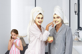 Little girl applying lipstick and two women applying face masks