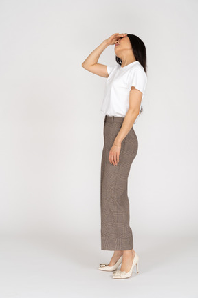 Side view of a young lady in breeches and t-shirt raising hear hand while looking up