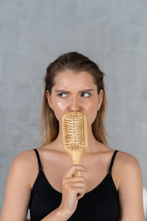 Front view of a young woman covering mouth with hairbrush