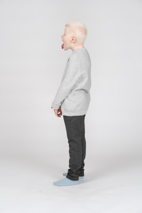 Side view of a kid boy in casual clothes showing tongue