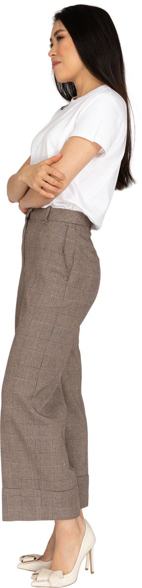 Vista lateral de uma jovem desconfiada de calça e camiseta cruzando as mãos