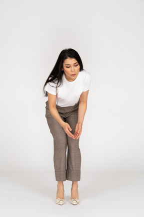 Front view of a questioning young lady in breeches and t-shirt raising hands and bending down